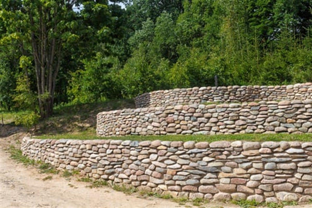 Curved natural stone retaining wall holding a graded slope with mature trees behind